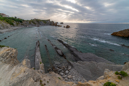 Beautiful sunset over Playa de la ArnÃ­a, featuring dramatic skies, rocky shoreline, and coastal homes in Cantabria, Spain. Perfect for seascape, travel, and nature themes.の写真素材