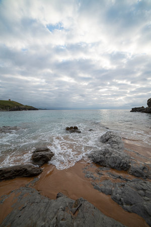 Tranquil scene of Tagle Beach in Cantabria, Spain, showcasing rugged rocks, gentle waves, and an expansive horizon. Perfect for travel, nature, and coastal themes.の写真素材