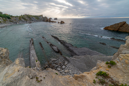 Beautiful sunset over Playa de la ArnÃ­a, featuring dramatic skies, rocky shoreline, and coastal homes in Cantabria, Spain. Perfect for seascape, travel, and nature themes.の写真素材