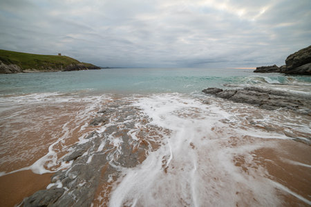Tranquil scene of Tagle Beach in Cantabria, Spain, showcasing rugged rocks, gentle waves, and an expansive horizon. Perfect for travel, nature, and coastal themes.の写真素材