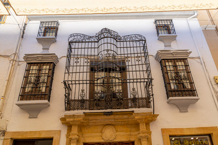 A quaint balcony with ornate iron railings and closed wooden shutters, set against a pastel green wall in Ronda, Spain. Perfect for themes of Mediterranean architecture and rustic charmの写真素材