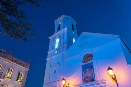 A beautifully lit church tower against the deep blue evening sky in Nerja, Spain. Ideal for travel, architecture, or cultural themes showcasing European landmarks.の写真素材