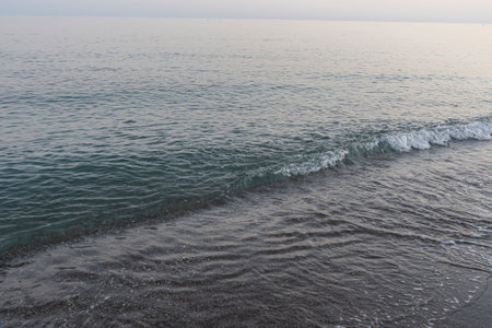 Gentle waves lap the shore at dusk on a tranquil beach in MÃ¡laga, Spain. Perfect for themes of relaxation, coastal serenity, and nature's beauty.の写真素材