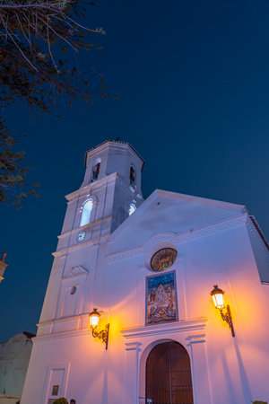 A beautifully lit church tower against the deep blue evening sky in Nerja, Spain. Ideal for travel, architecture, or cultural themes showcasing European landmarks.の写真素材