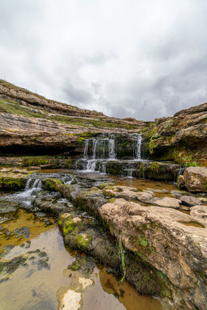 Picturesque waterfall flowing over layered rock formations with lush green moss in Cantabria, Spain. Ideal for nature, travel, and landscape themes.の写真素材