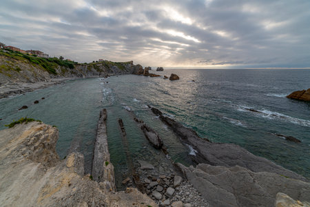 Beautiful sunset over Playa de la ArnÃ­a, featuring dramatic skies, rocky shoreline, and coastal homes in Cantabria, Spain. Perfect for seascape, travel, and nature themes.の写真素材