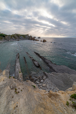 Beautiful sunset over Playa de la ArnÃ­a, featuring dramatic skies, rocky shoreline, and coastal homes in Cantabria, Spain. Perfect for seascape, travel, and nature themes.の写真素材