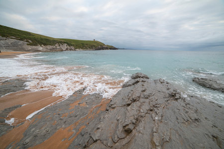 Tranquil scene of Tagle Beach in Cantabria, Spain, showcasing rugged rocks, gentle waves, and an expansive horizon. Perfect for travel, nature, and coastal themes.の写真素材