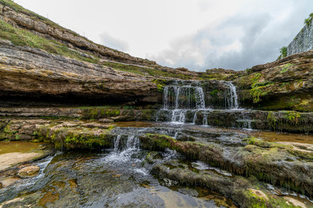 Picturesque waterfall flowing over layered rock formations with lush green moss in Cantabria, Spain. Ideal for nature, travel, and landscape themes.の写真素材