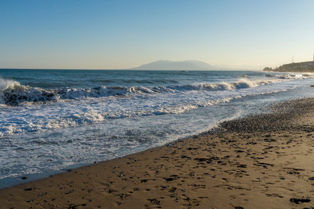 Powerful waves break along the shores of Malaga, Spain, with distant mountains visible on the horizon. Ideal for themes of coastal energy, nature, and scenic seascapesの写真素材