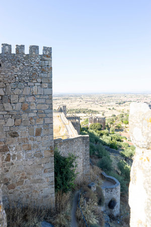 Stone walls of a historic fortress rise against the bright blue sky in Trujillo, Extremadura. The vast landscape stretches out, showcasing rolling hills, greenery, and distant ruins.の写真素材