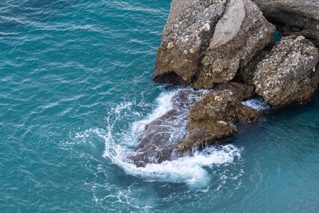 Clear turquoise waters crash against rugged rocks along the coastline of Malaga, Spain, showcasing...