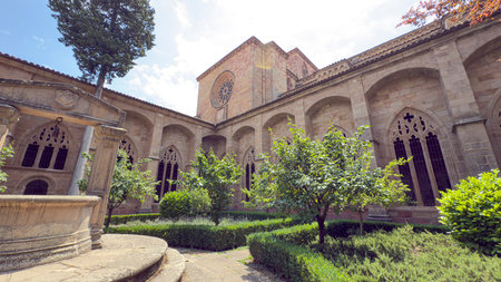 Visitors admire the stunning design of Cathedral of Porquenza in Spain, framed by lush greenery and elegant stone architecture on a sunny day, creating a tranquil atmosphere.の写真素材