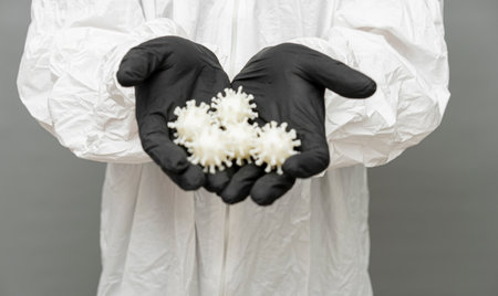 Hands in nitrile gloves hold virus models, showcasing the detailed study of covid-19. This...
