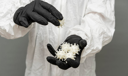 Experts wearing nitrile gloves hold model representations of the Covid-19 virus, illustrating the...