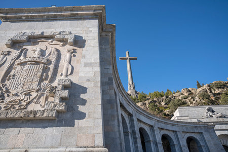 Monument with cross and stone carvings under blue sky. Valley of the Fallen, landscape