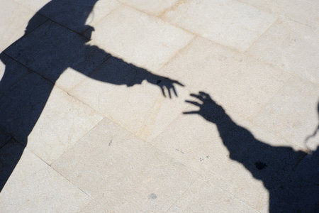 Shadows of two hands reaching out on sunlit pavement.の写真素材