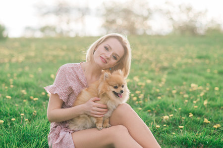 Attractive young woman holding dog spitz outside and smiling at camera, walking in the park. Concept about friendship between people and animals.の写真素材