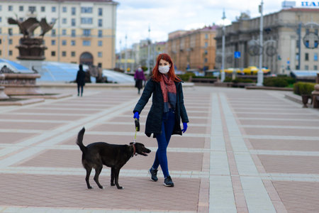 Young female using a face mask as a coronavirus spreading prevention walking with her dog. Global COVID-19 pandemic conception, animalsの写真素材