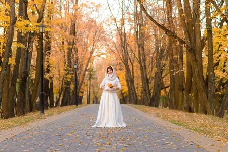 Portrait of a beautiful young redhead girl with flowers look attractive in a white dress on a background of autumn forest and leaves smiling.の写真素材