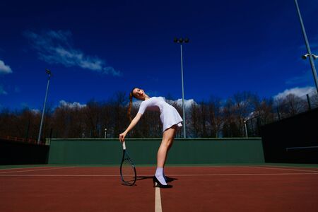 Sexy girl tennis player in white dress and heels holding tennis racket on the court.の写真素材