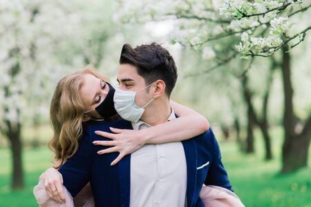 Young loving couple walking in medical masks in the park during quarantine on their wedding day. Coronavirus, disease, protection, sick. Europe celebration canceled.の写真素材