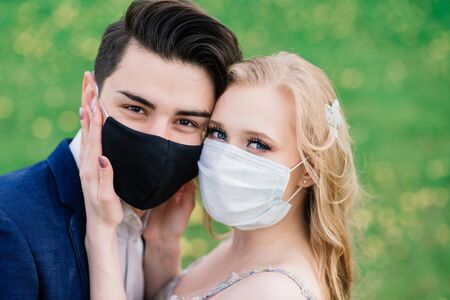 Young loving couple walking in medical masks in the park during quarantine on their wedding day. Coronavirus, disease, protection, sick. Europe celebration canceled.の写真素材