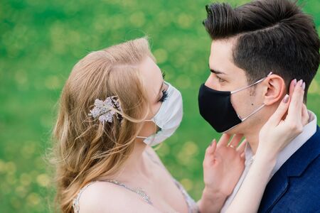 Young loving couple walking in medical masks in the park during quarantine on their wedding day. Coronavirus, disease, protection, sick. Europe celebration canceled.の写真素材