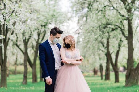 Young loving couple walking in medical masks in the park during quarantine on their wedding day. Coronavirus, disease, protection, sick. Europe celebration canceled.の写真素材