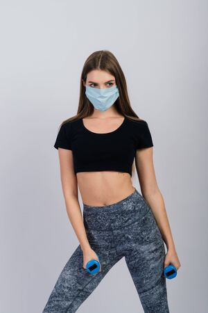 Young woman in a protective mask with dumbbells on a white background. Quarantined sportsの写真素材