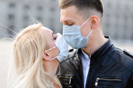 Couple wears a medical mask walking on the street of the city during the spread of news about the epidemic of coronavirus. Love story.の写真素材