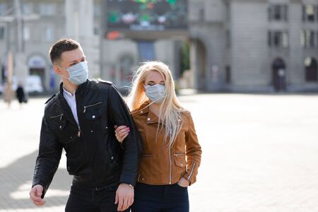 Couple wears a medical mask walking on the street of the city during the spread of news about the epidemic of coronavirus. Love story.の写真素材