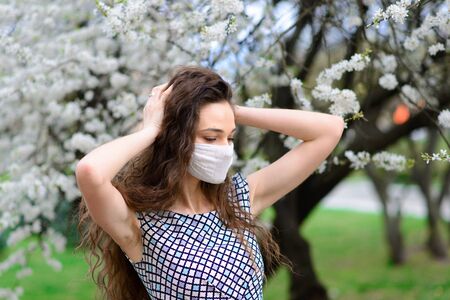Girl, young woman in a protective sterile medical mask on her face in the spring garden. Pollution, virus, pandemic coronavirus concept.の写真素材