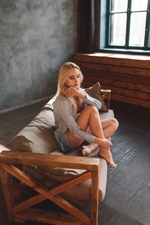 Sexy beautiful blonde posing in black lingerie and a white shirt in interior studioの写真素材