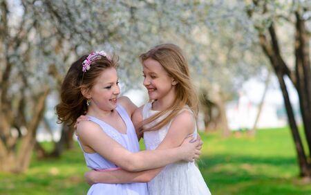 Two beautiful young girls with blue eyes in a white dresses in the garden having fun and enjoying smell of flowering spring garden.の写真素材