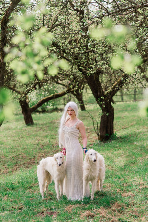 Blonde woman in white dress playing with her russian wolfhound dog in garden