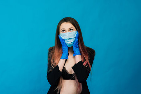 Cheerful and joyful young female playing with protective medical mask and gloves on blue background....