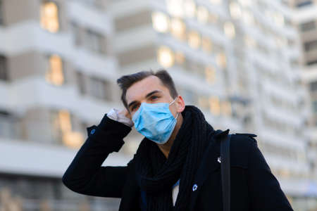 Portrait of young handsome businessman with face mask in quarantine of flu. Photo in caffee with laptop, mobile phone. Coronavirus pandemic.の写真素材