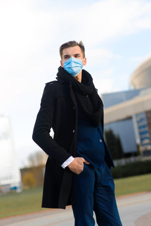 Portrait of young handsome businessman with face mask in quarantine of flu. Photo in caffee with laptop, mobile phone. Coronavirus pandemic.の写真素材