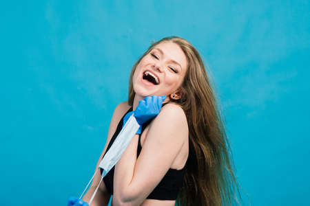 Fitness girl wearing medicine mask in fitness costume isolated on blue background. Training during quarantine, covid 19, corona virus.の写真素材