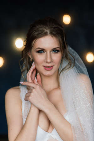 Beautiful bride in white lace lingerie, with bare shoulder sitting in a hotel room, boudoir. Happy wedding morning.の写真素材