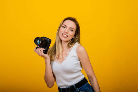 Excited female photographer working in studio. Portrait of stunning blonde girl with camera.の写真素材