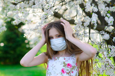 Lonely teenage girl wearing protection medicine mask against virus covid and allergy enjoying spring flower blossom in blooming gardenの写真素材