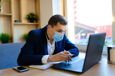 Portrait of young handsome businessman with face mask in quarantine of flu. Photo in caffee with...