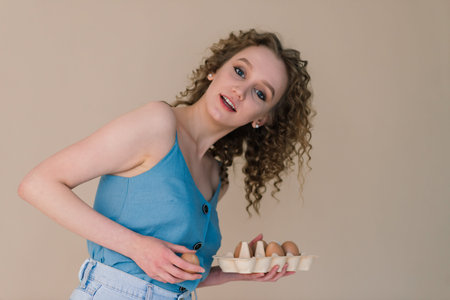 Studio shot of a cute curly woman holding an eggs - copy space on grey background. Emotional...