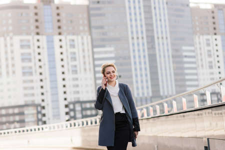 Lawyer businesswoman professional walking outdoors talking on cell smart phone drinking coffee from disposable paper cup.の写真素材