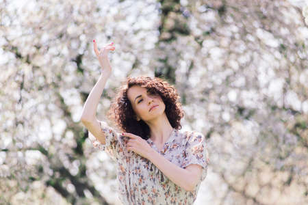 Young attractive woman with curly long hair posing in spring blooming gardenの写真素材