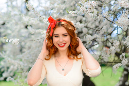 Portrait of beautiful red-haired young woman in white dress in spring flowersの写真素材