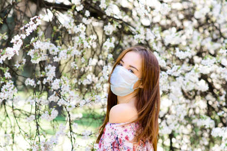 Girl, young woman in a protective sterile medical mask on her face in the spring garden. Pollution, virus, pandemic coronavirus concept.の写真素材