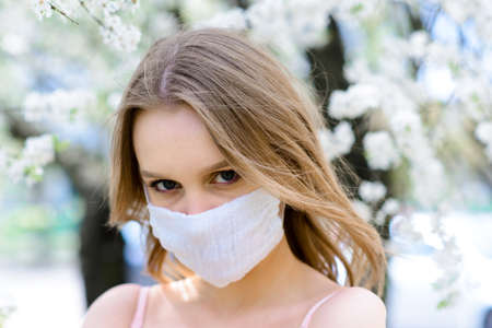 Girl, young woman in a protective sterile medical mask on her face in the spring garden. Pollution, virus, pandemic coronavirus concept.の写真素材